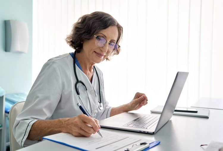 Senior female doctor in clinic consulting remotely using pc laptop computer.