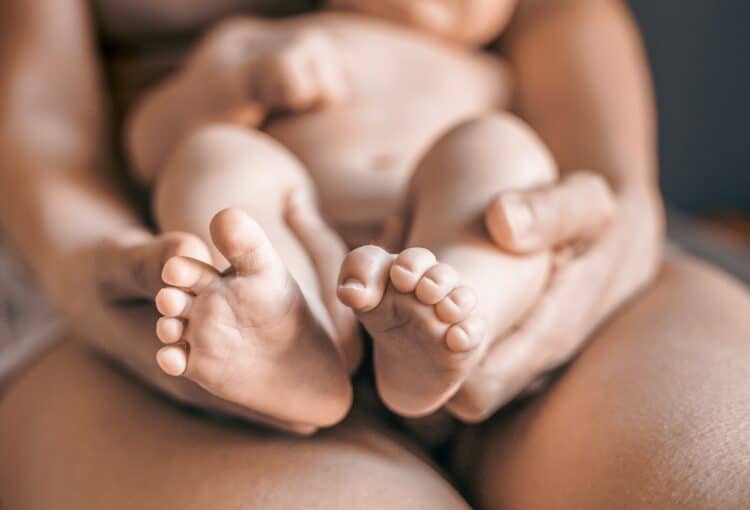 Mom, mummy, young mother with little baby daughter feet, legs in hands. Mum woman hugging child. New