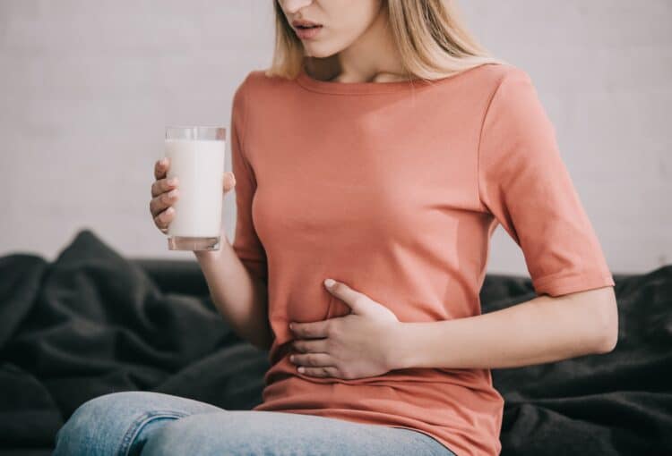 cropped view of blonde woman with lactose intolerance holding glass of milk while sitting on sofa