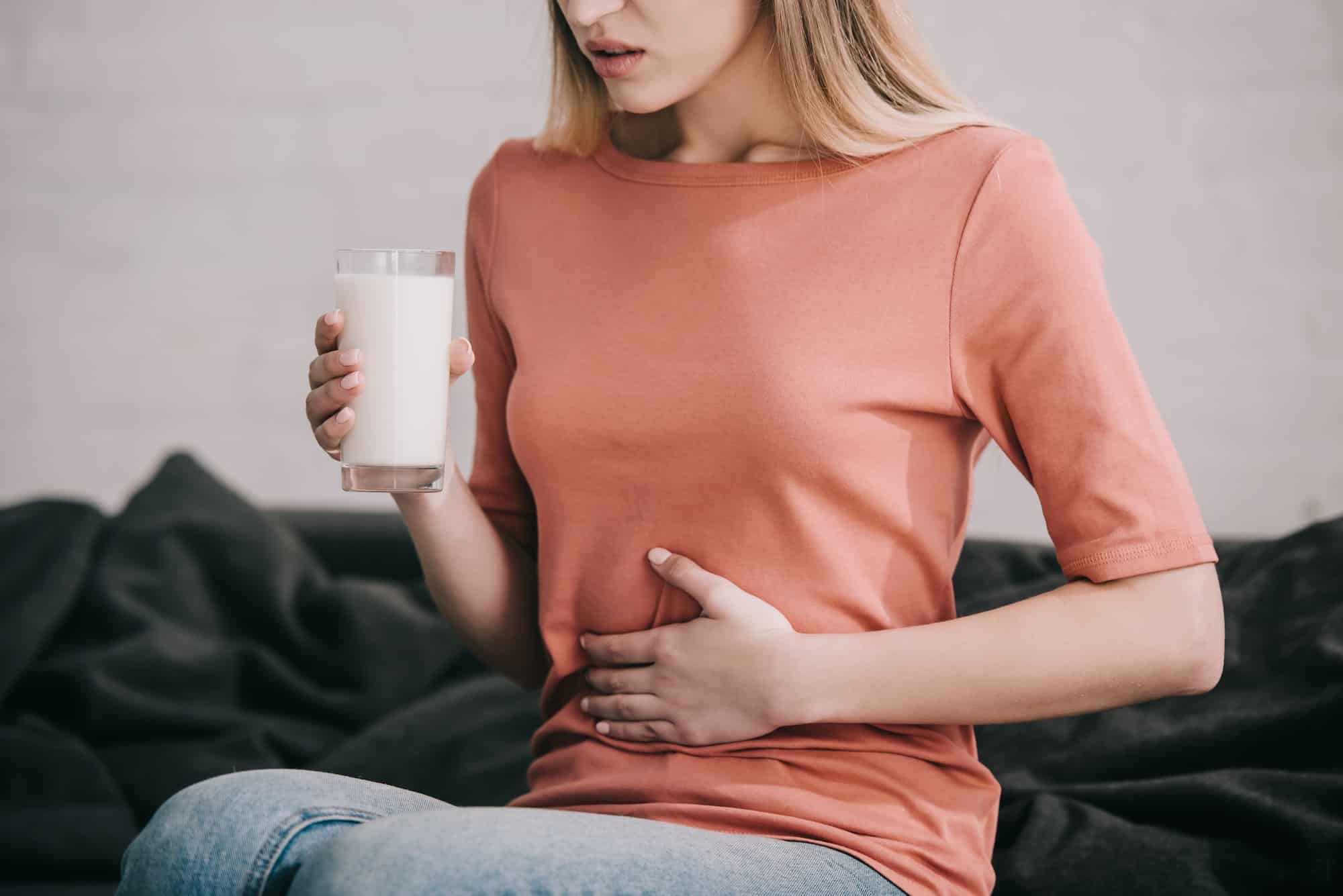 cropped view of blonde woman with lactose intolerance holding glass of milk while sitting on sofa