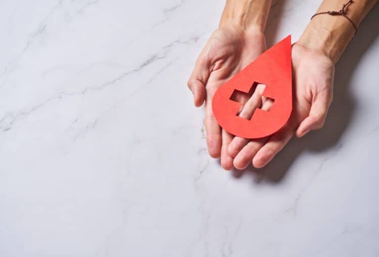 Hands holding a drop of blood. World Hemophilia Day