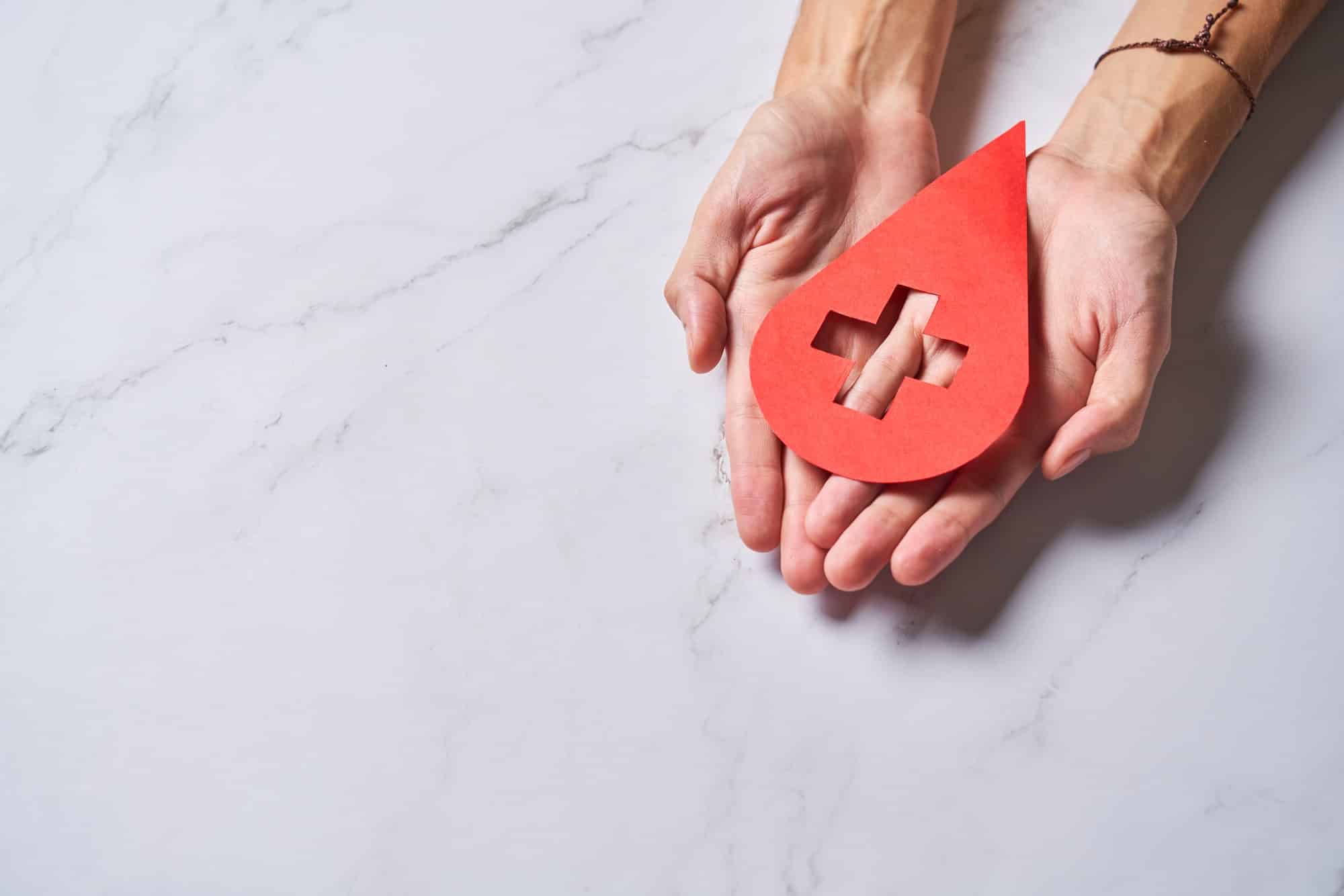 Hands holding a drop of blood. World Hemophilia Day