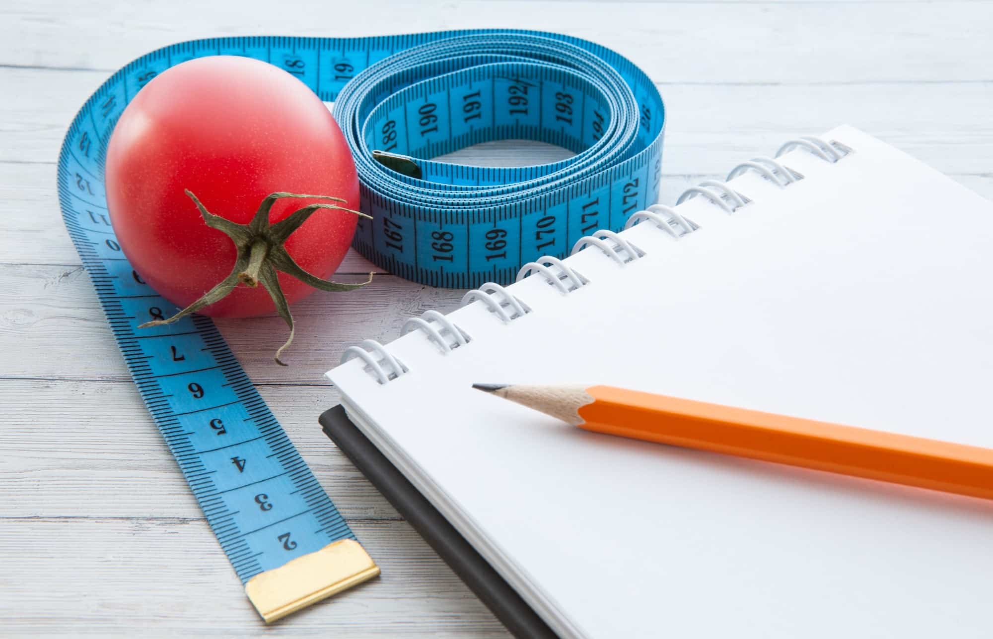 Measuring tape and notebook with juicy tomatoes, the concept of healthy eating and losing weight
