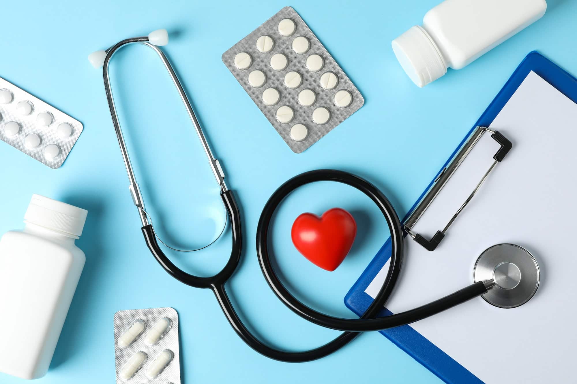 Stethoscope, tablet, heart and medicine on blue background, top view